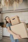 Side view of young woman making effort and carrying cardboard boxes with stuff in house — Stock Photo