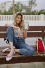 Donna allegra con tazza di caffè da asporto seduta sulla panchina della città sul lungomare il giorno d'estate — Foto stock