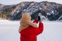 Vue arrière de Femme prenant des photos de montagnes enneigées avec smartphone — Photo de stock