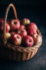 Manzanas rojas frescas sobre mesa oscura y en canasta de mimbre sobre fondo oscuro - foto de stock