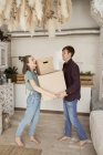 Вид сбоку на молодую пару, делающую усилие и несущую картонные коробки с вещами в доме — стоковое фото