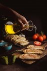 Невпізнаваний кухар наливає олію на шматочки свіжого хліба з соусом, готуючи тости на чорному тлі — стокове фото