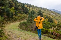 Back view of woman in yellow raincoat walking in forest — Stock Photo