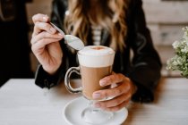 Обрізане зображення модної красивої блондинки, що п'є зі склянки смачної піни кави — стокове фото