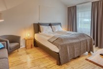 Quarto confortável com paredes de madeira branca e grande cama macia com sofá cinza aconchegante perto de lâmpada de assoalho ardente — Fotografia de Stock
