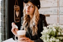 Longo cabelo na moda bela mulher loira bebendo de um copo de delicioso café espumoso, olhando para a câmera — Fotografia de Stock