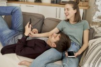 Спокойный вдумчивый молодой человек и женщина, лежащие на уютном мягком диване и серфинг мобильных телефонов дома — стоковое фото