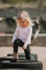 Happy joyful little girl having fun and walking through row of black car tires while playing outdoors on summer day — Stock Photo