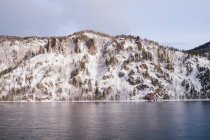 Paisagem fascinante surpreendente de rio siberiano livre de gelo largo com água calma escura e montanhas cobertas de neve no dia de inverno nublado — Fotografia de Stock