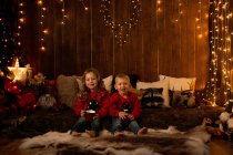 Adorable petite fille et garçon assis dans la chambre pleine de décoration de Noël, regardant à la caméra — Photo de stock