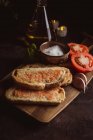 Специи, чеснок и помидоры рядом с тостами на деревянной доске — стоковое фото