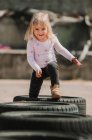 Felice gioiosa bambina divertirsi e camminare attraverso la fila di pneumatici auto nere mentre si gioca all'aperto il giorno d'estate — Foto stock