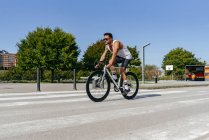 Спортсмен їде на велосипеді на проїжджій частині міста з зеленими деревами на узбіччі в літній день з блакитним небом — стокове фото