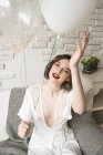 Alto angolo di splendida donna felice seduta sul divano e che tiene palloncini in appartamento leggero in stile loft — Foto stock