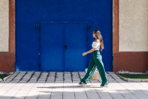 Jeune femme heureuse et branchée marchant en ville contre la porte bleue — Photo de stock