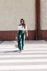 Stylisch lächelnde Frau mit Sonnenbrille und Handtasche beim Überqueren der Straße — Stockfoto