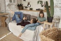 Calmo pensativo jovem e mulher deitada no sofá macio aconchegante e surfar telefones celulares em casa — Fotografia de Stock