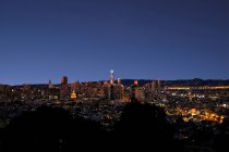 Вид с беспилотника на освещенный столичный город с небоскребами против безоблачного темно-синего неба ночью — стоковое фото