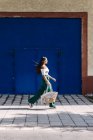 Jeune femme heureuse et branchée marchant en ville contre la porte bleue — Photo de stock