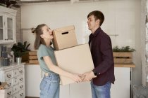 Side view of young couple making effort and carrying cardboard boxes with stuff in house — Stock Photo
