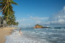 Giovane donna in acqua sulla spiaggia di sabbia con foresta tropicale — Foto stock