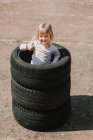 From above of happy adorable little girl standing in stack of car tires doing the ok sign while having fun and playing outdoors on summer day — Stock Photo