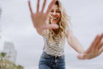 From below of joyful laughing woman in casual clothes spreading hands and hiding face from camera while walking in city — Stock Photo