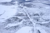 Vue par drone d'une étroite route sinueuse traversant des champs enneigés et des forêts dans la nature — Photo de stock