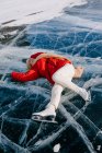From above of happy young active female in warm active wear and skates lying on ice on frozen river and enjoying nice winter day in Siberia — Stock Photo
