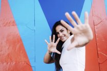 Портрет молодої усміхненої жінки жестикулює руками, дивлячись на камеру проти кольорової стіни — стокове фото