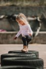 Feliz menina alegre se divertindo e andando através da linha de pneus de carro preto enquanto joga ao ar livre no dia de verão — Fotografia de Stock