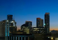 Вид с беспилотника на освещенный столичный город с небоскребами против безоблачного темно-синего неба ночью — стоковое фото