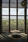 Salón con mesa redonda de madera y silla de metal contra ventanas altas con rejilla en contraste en la biblioteca Texas - foto de stock
