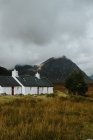 Granja blanca solitaria en campo de otoño en valle en Escocia rodeada de colinas rocosas - foto de stock