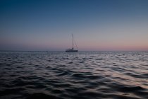 Vista laterale della barca a vela che scorre su acque calme del mare al tramonto — Foto stock