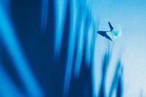 Крихкий синій метелик з паперу з тіні листя пальми, прикріпленої до синьої шовкової тканини — стокове фото