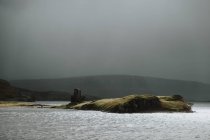 Paysage de petite île près de la côte écossaise pendant la journée orageuse avec des collines brumeuses et des ruines de château — Photo de stock