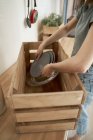 Mains de femme en vêtements décontractés emballant la vaisselle à la maison dans une boîte en bois au comptoir dans la cuisine — Photo de stock