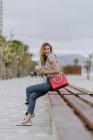 Attraente donna moderna con un bel sorriso indossando camicia a righe casual guardando lontano mentre seduto in panchina — Foto stock