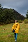 Visão traseira da mulher em capa de chuva amarela andando na floresta — Fotografia de Stock