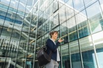 Low angle of happy businesswoman holding hand in pocket and using smartphone while standing outside business center on city street — Stock Photo