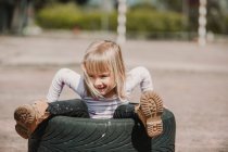 Сверху счастливая очаровательная маленькая девочка сидит внутри шины автомобиля, веселясь и играя на открытом воздухе в летний день — стоковое фото