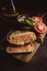 Різні спеції і стиглі помідори кладуть на обробну дошку біля шматків хліба з соусом на столі — стокове фото