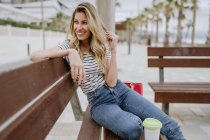 Seitenansicht einer Frau, die an einem Sommertag auf einer Bank am Meer sitzt und wegschaut — Stockfoto