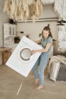 Poderosa jovem alegre tentando transportar máquina de lavar roupa branca sozinho na cozinha leve — Fotografia de Stock