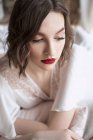 Splendida donna con labbra rosse in abito bianco guardando altrove mentre seduto sul pavimento accanto al divano — Foto stock