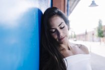 Jovem sorrindo mulher encostada a uma parede azul olhando para baixo — Fotografia de Stock