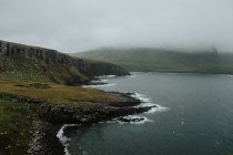 Paisagem selvagem de colinas nebulosas e oceano com ondas batendo em rochas na costa na Escócia — Fotografia de Stock