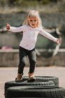 Счастливая веселая девчонка веселится и гуляет по рядам черных автомобильных шин, играя на свежем воздухе в летний день — стоковое фото