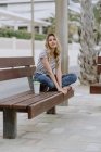 Selbstbewusste, lässige Frau, die an einem Sommertag auf einer Bank am Meer sitzt und in die Kamera blickt — Stockfoto